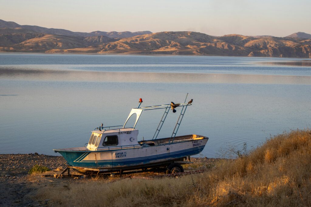 A fishing boat rests on the shore of Keban Dam Lake in ElazΔ±Δ, TΓΌrkiye during sunset.