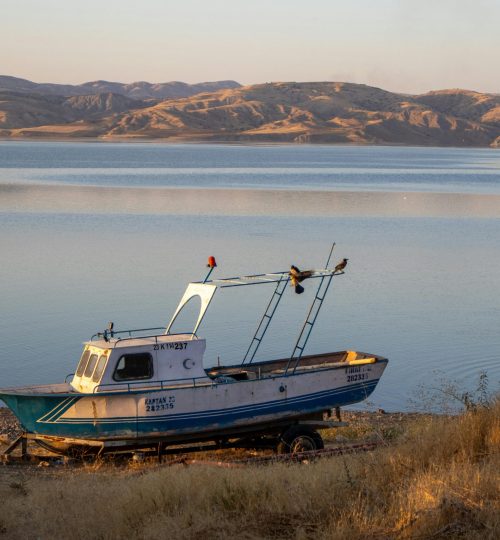 A fishing boat rests on the shore of Keban Dam Lake in Elazığ, Türkiye during sunset.